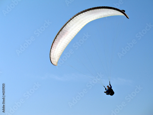 A paraglider il flying in the blue sky with his white paraglide