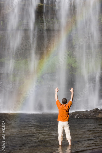 Man standing of a tropical waterfall with rainbow - Brazil