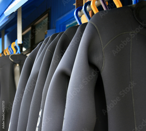 A row of wetsuits hanging up to dry photo
