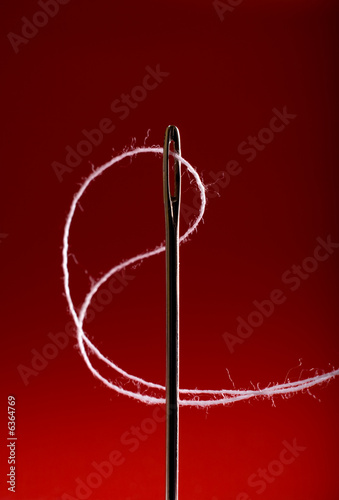 Macro of needle with white thread against red background.