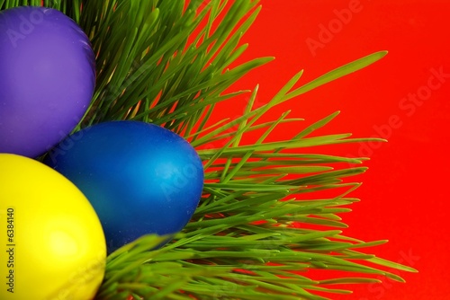 Easter holiday. Color eggs on the grass on red background.