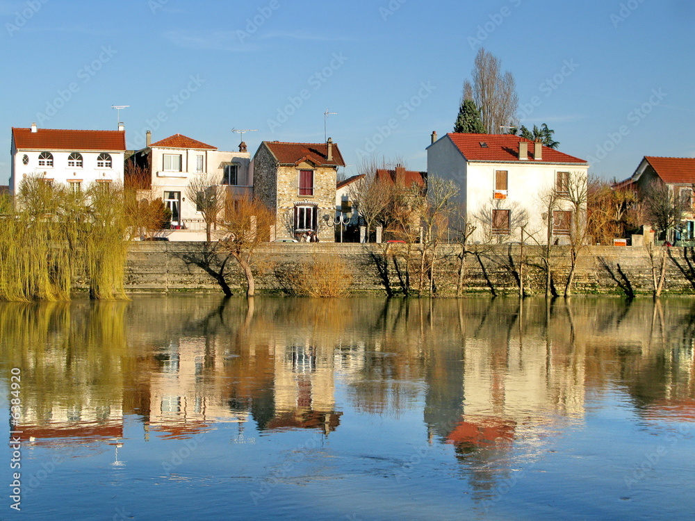 Maisons et saules pleureurs se reflétant dans le fleuve.