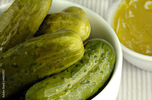 Pickled cucumbers arranged in a white dish with mustard.