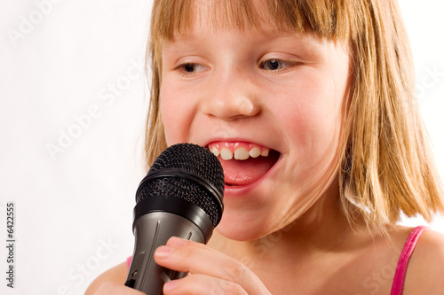 Pretty litle girl singing in microphone isolated over white