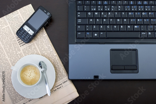 Office desk with laptop computer, newspapers, phone and coffee