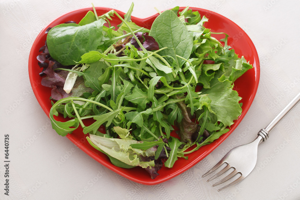 fresh leaf salad on red heart shape plate with fork on the table