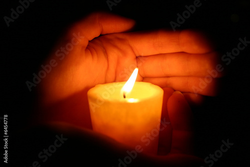 hands keeps burninging candle in the dark