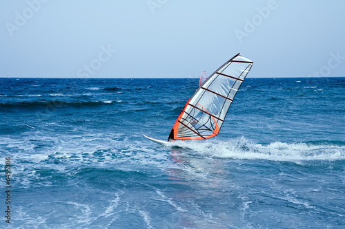 windsurfer sailing away form the beach on blue waters