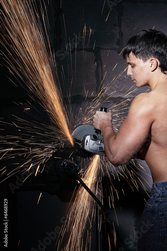 Muscular worker cuts metal with sparks. Circular metal cutter.