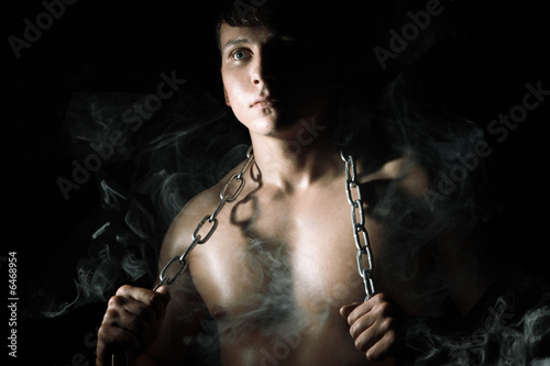 Muscular man with chain and smoke. Night in the conclusion