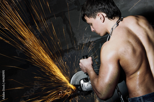 Muscular worker cuts metal with sparks. Circular metal cutter.