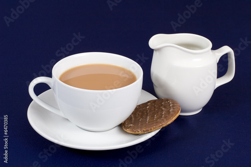 A cup of tea with a chocolate biscuit and milk jug