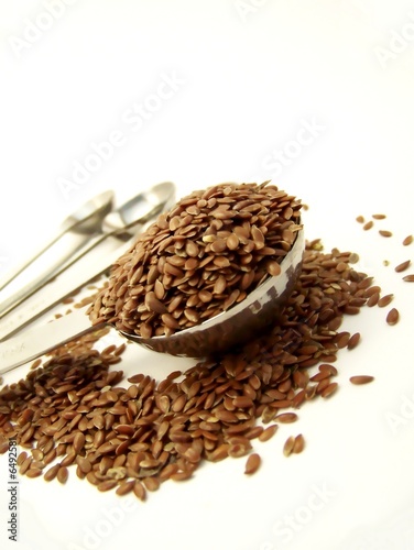 Angled image of whole flax seed overflowing a measuring spoon