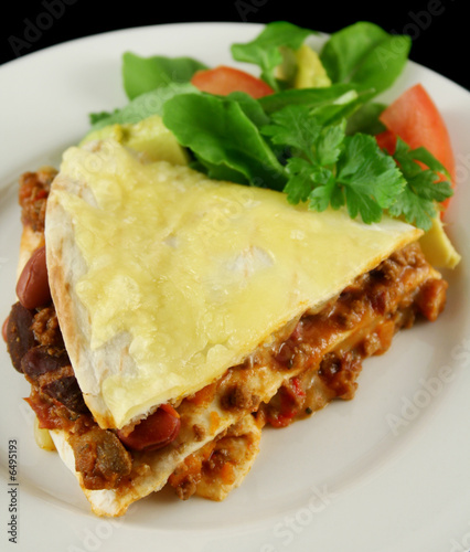 A slice of beef and bean Mexican tortilla stack with cheese 