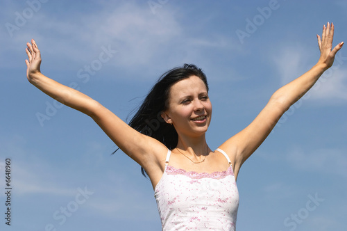 The cheerful girl with hands on a background of the blue sky.