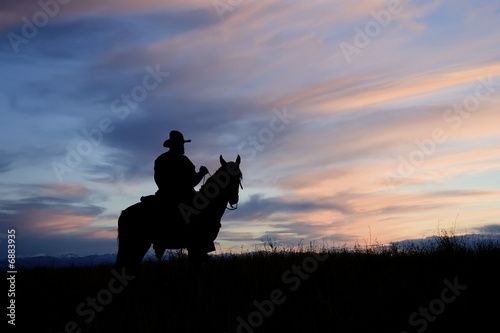 Cowboy on horseback back lit by the dawn sky