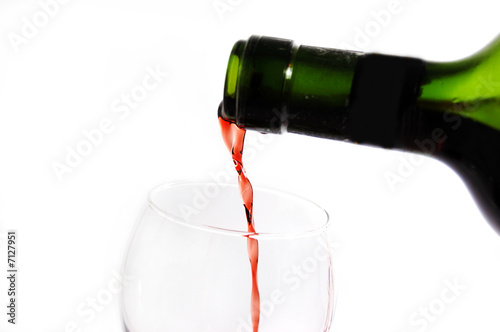 Green bottle pouring red wine into wineglass  over white photo