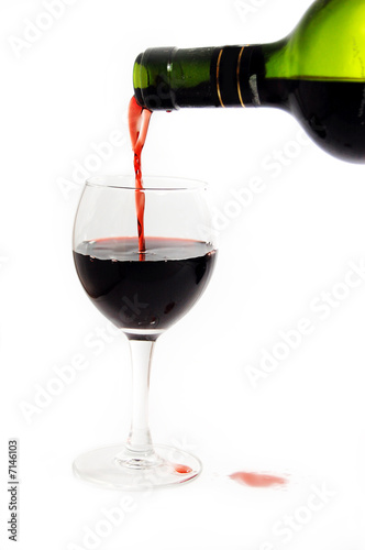 Green bottle pouring red wine into wineglass  over white