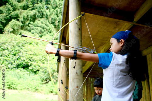 Young girl poised with bow and arrow, 