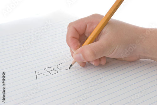 Child's hand holding pencil, writing alphabet on paper