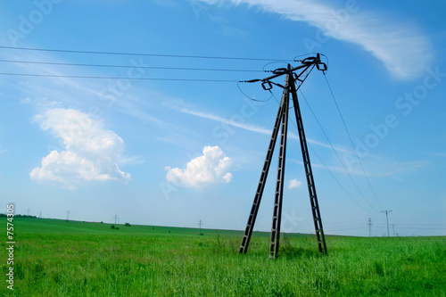 Old electric pylon on green grass against blue sky