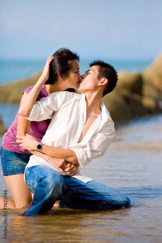 loving young couple kissing while squating by the beach