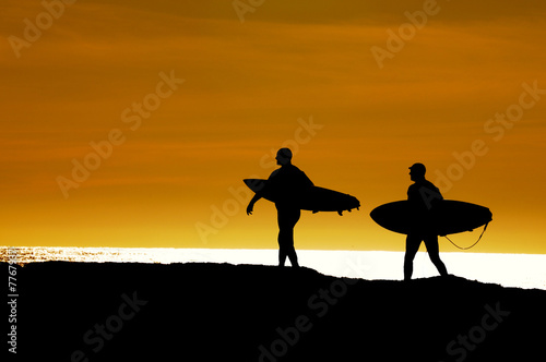 Pair of surfers heading out in the sunset
