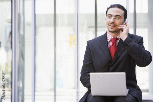 Businessman using laptop and mobile phone outside © Monkey Business
