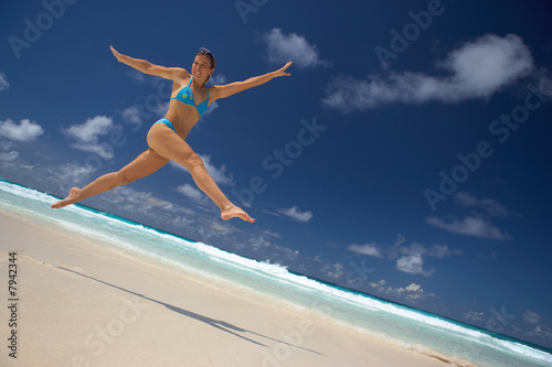 young woman jumping for joy on sandy beach