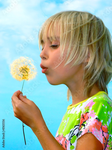 Little girl blows on a seedy pod plant as seeds drift off