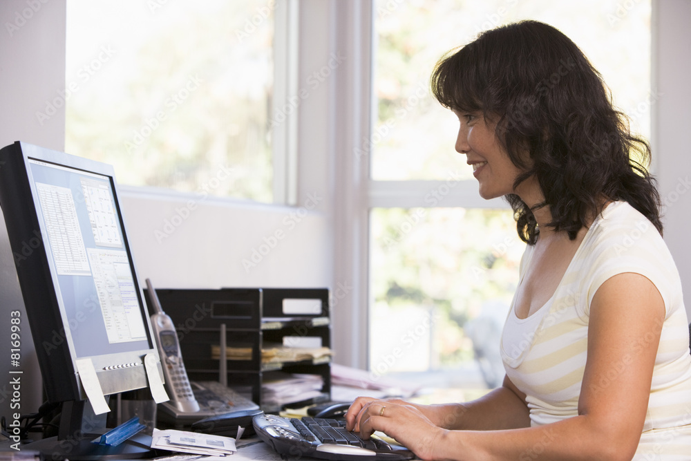 Woman in home office using computer and smiling Woman in home office using computer and smiling