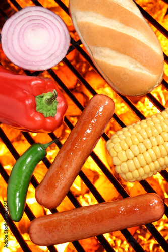 Hot dogs, bun, peppers, onion and corn on a barbecue grill