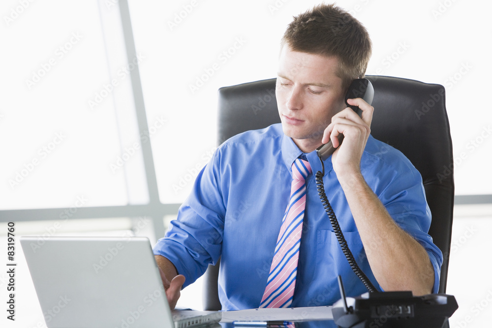 Businessman sitting in office with laptop on telephone Businessman sitting in office with laptop on telephone