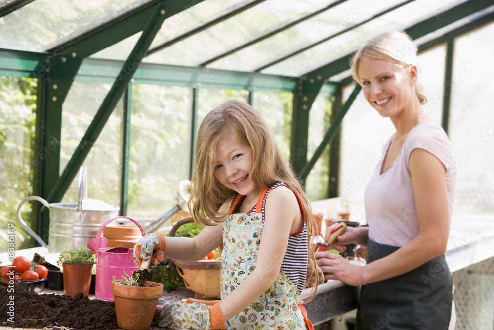 Fototapeta premium Young girl and woman in greenhouse putting soil in pots smiling