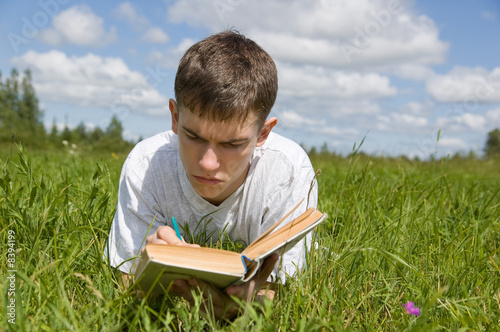 A young man reads a book, lying on a grass.
