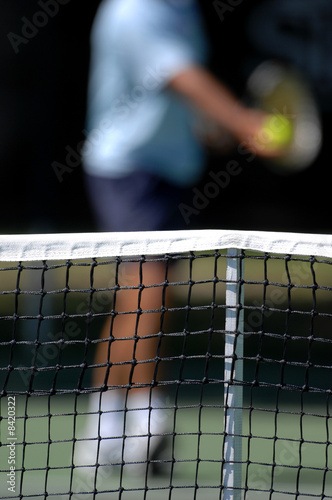 a net with a tennis player preparing to serve in the background © Sportlibrary