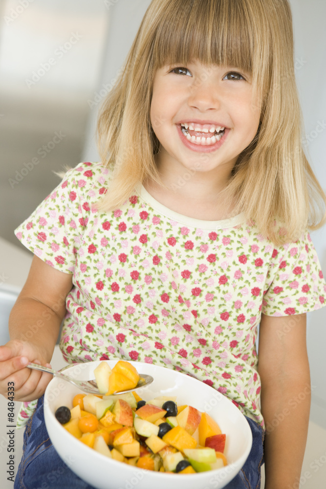 Young girl in kitchen eating bowl of fruit smiling Young girl in kitchen eating bowl of fruit smiling