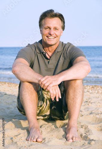 A portrait of a happy 44 year old man sitting on beach. photo