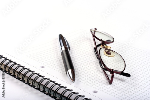 Notepad with eyeglasses and pen isolated on white