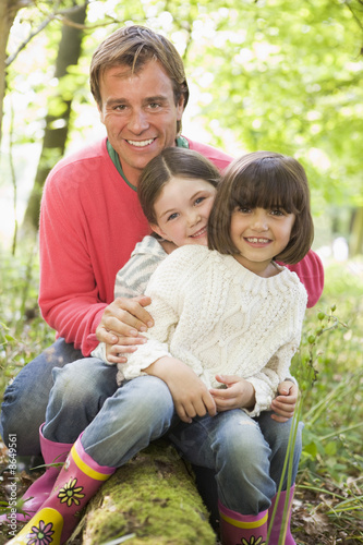 Father and daughters outdoors in woods sitting on log smiling © Monkey Business