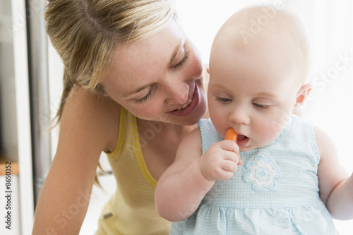 Mother and baby in kitchen eating carrot
