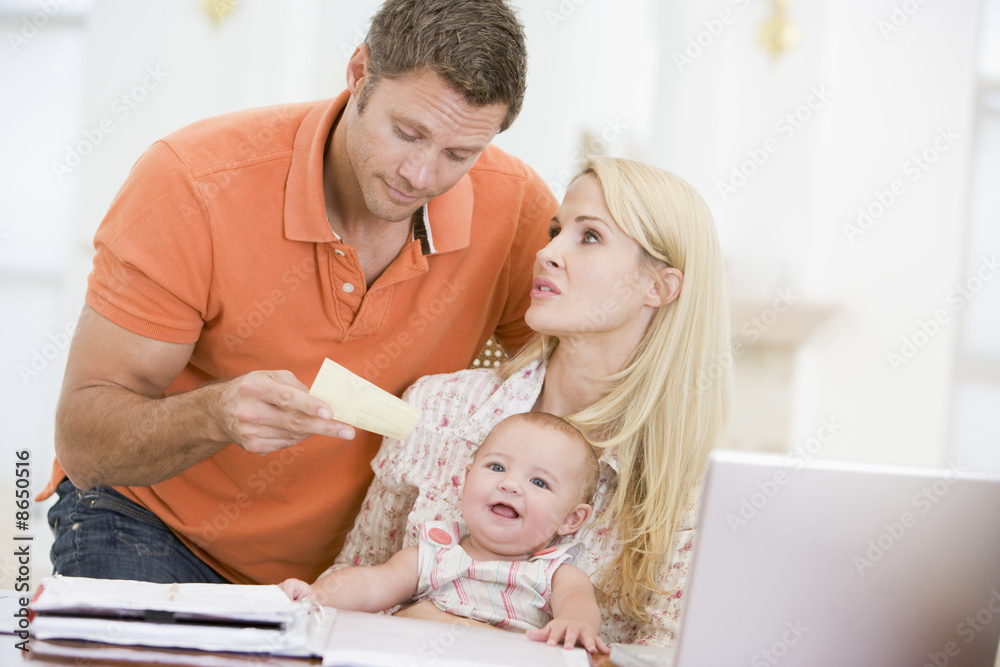 Couple and baby in dining room with laptop and paperwork Couple and baby in dining room with laptop and paperwork
