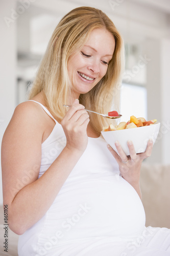 Pregnant woman with bowl of fruit salad smiling