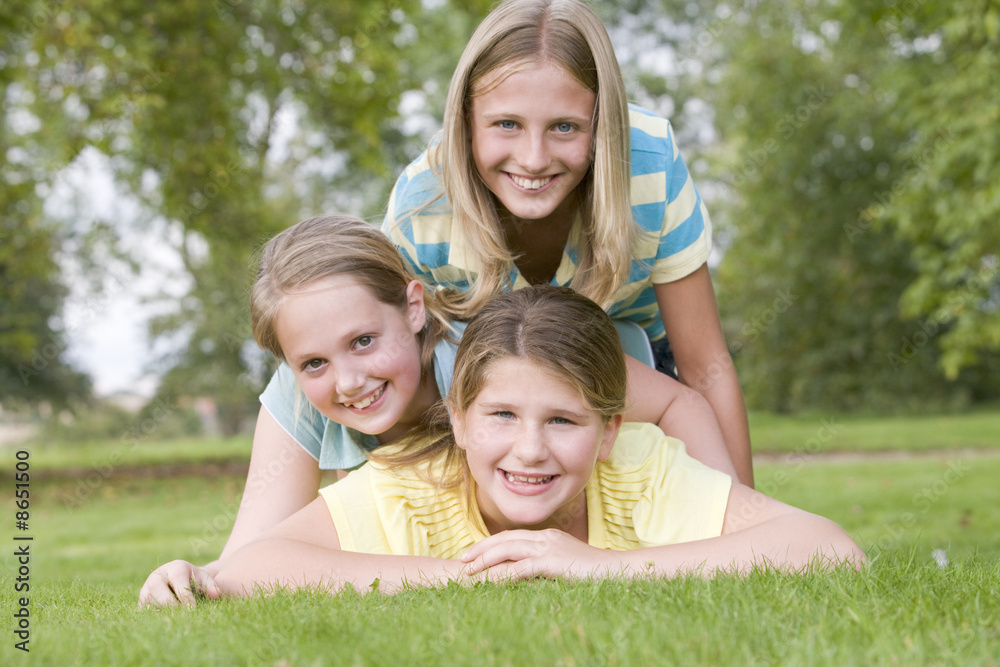 Three young girl friends piled on each other outdoors smiling Three young girl friends piled on each other outdoors smiling