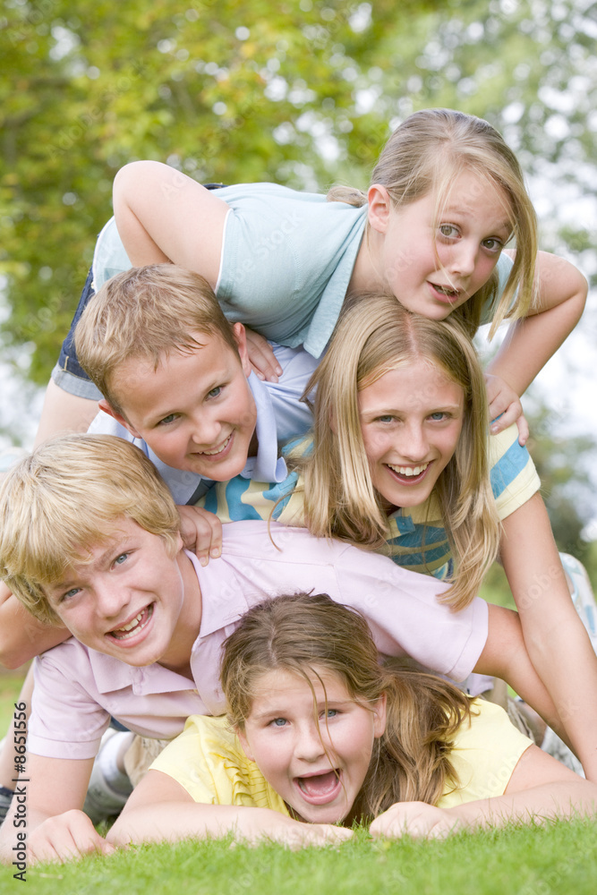 Five young friends piled on each other outdoors smiling