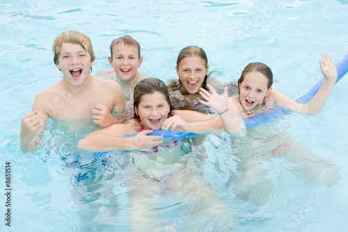 Five young friends in swimming pool playing and smiling