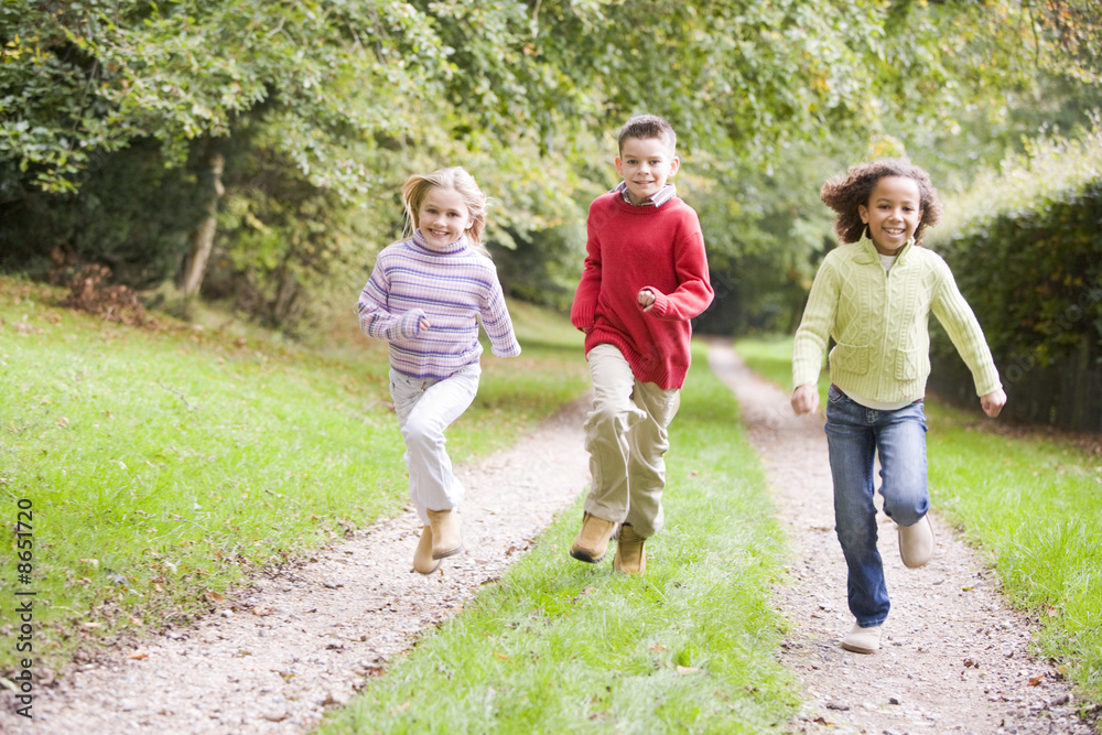 Fototapeta premium Three young friends running on a path outdoors smiling