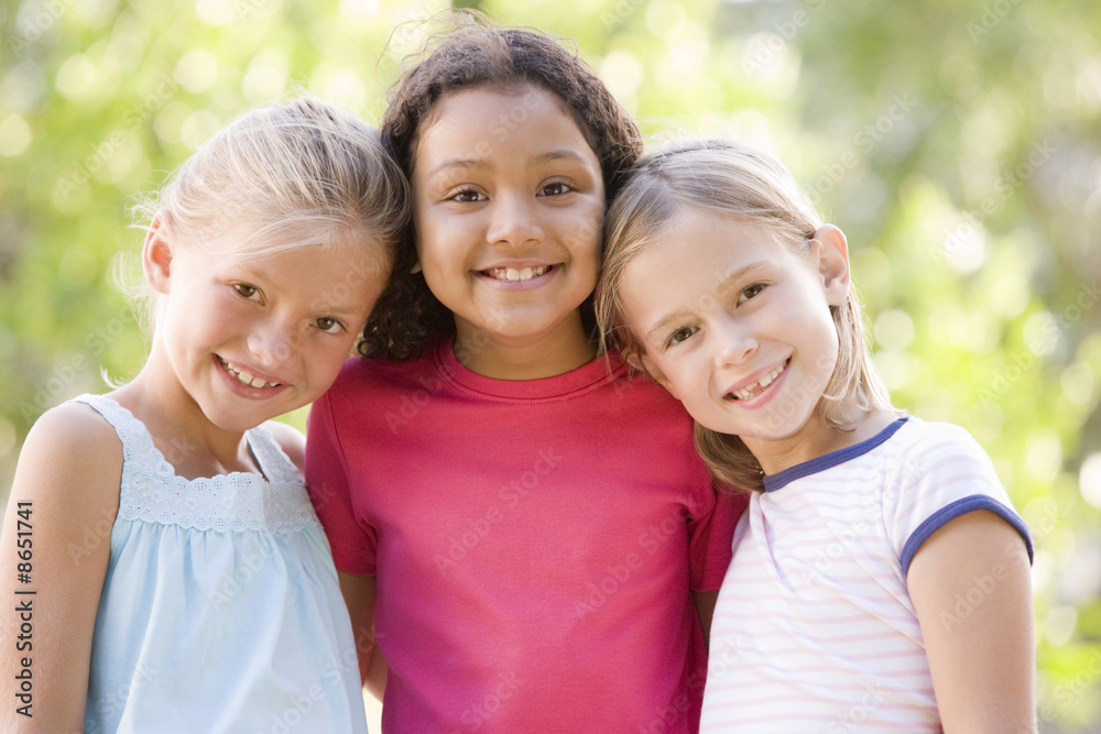 Fototapeta premium Three young girl friends standing outdoors smiling
