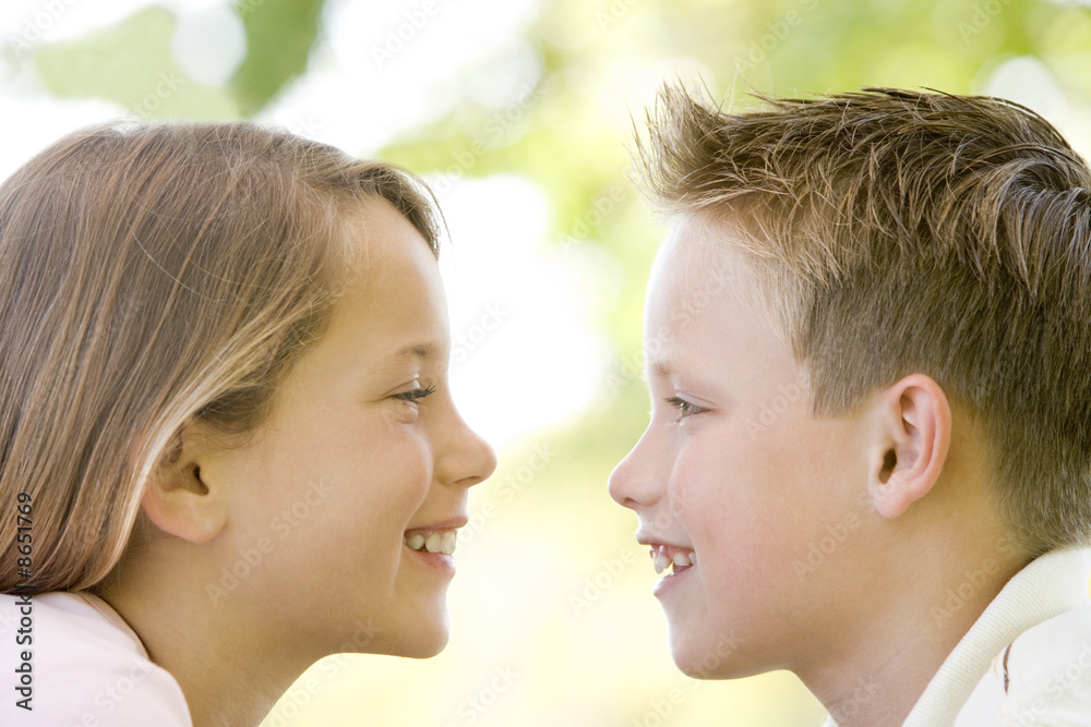 Brother and sister sitting outdoors staring at each other and sm Brother and sister sitting outdoors staring at each other and sm