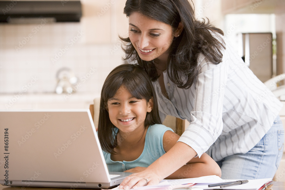 Woman and young girl in kitchen with laptop and paperwork smilin Woman and young girl in kitchen with laptop and paperwork smilin